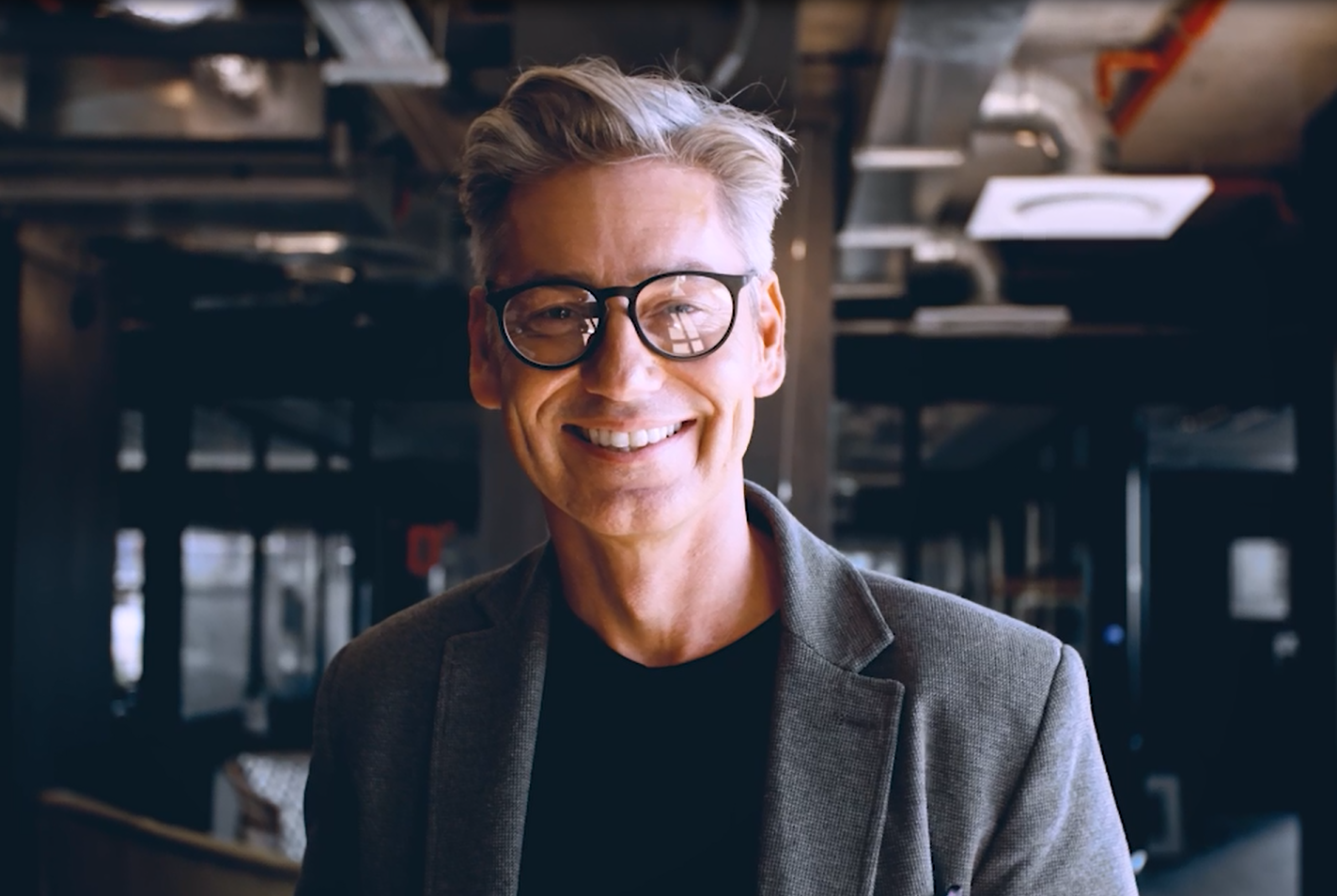 ein Mann mit grauen Haaren und Brille lacht in die Kamera